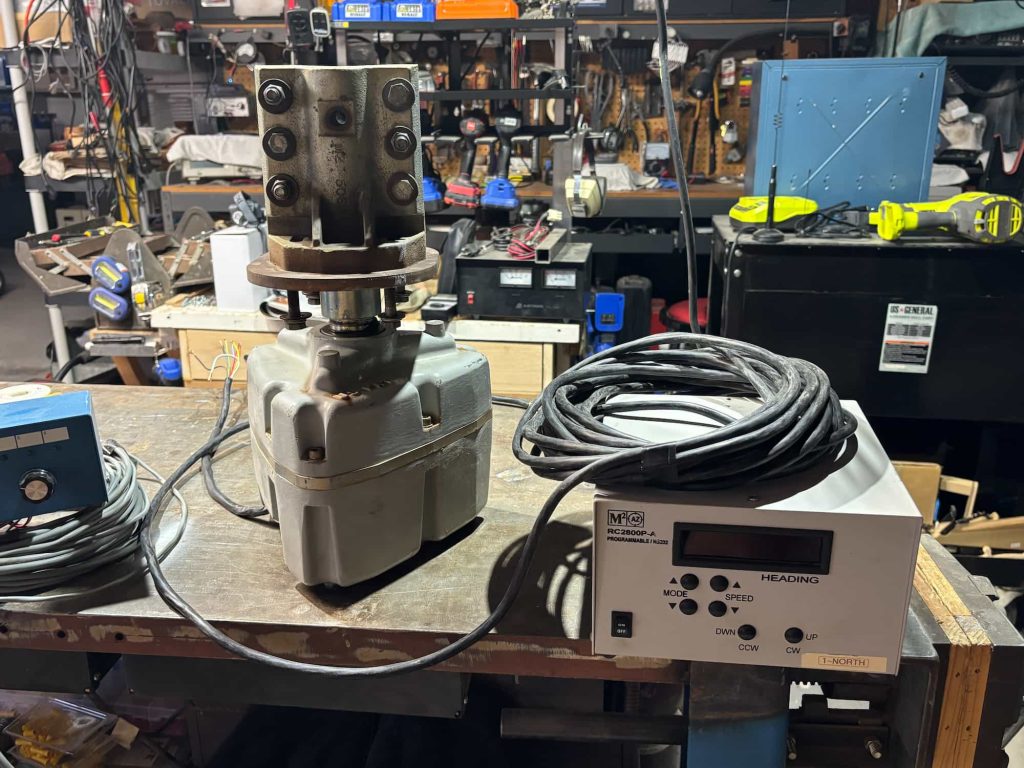 Industrial equipment in a cluttered workshop. A motor with cables is attached to a control box on a wooden workbench. Tools and shelves are visible in the background.