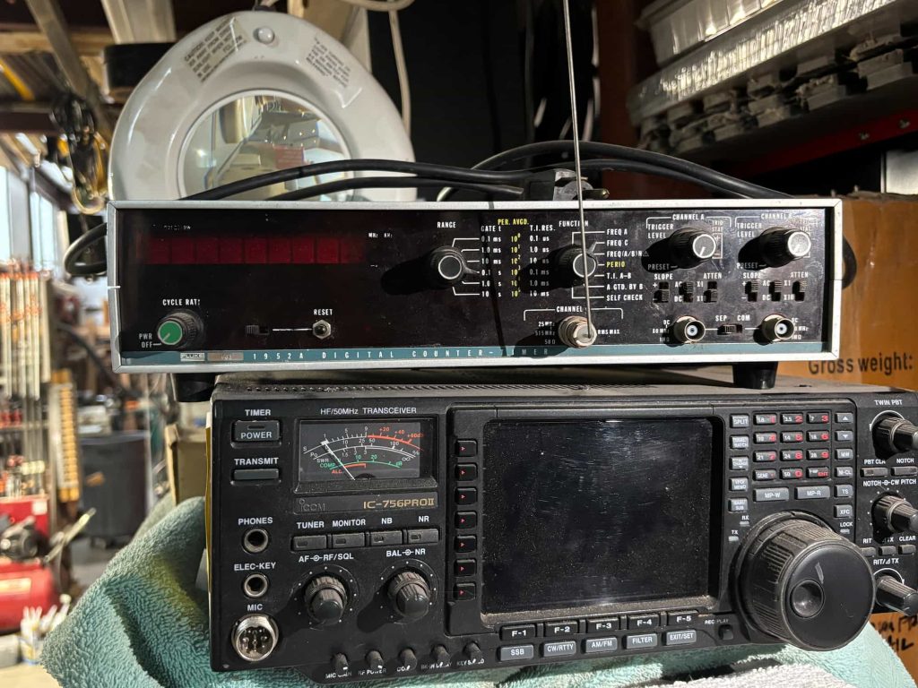 A vintage radio transceiver sits below a digital counter on a cluttered shelf. The scene conveys a sense of nostalgia and technical hobbyism.